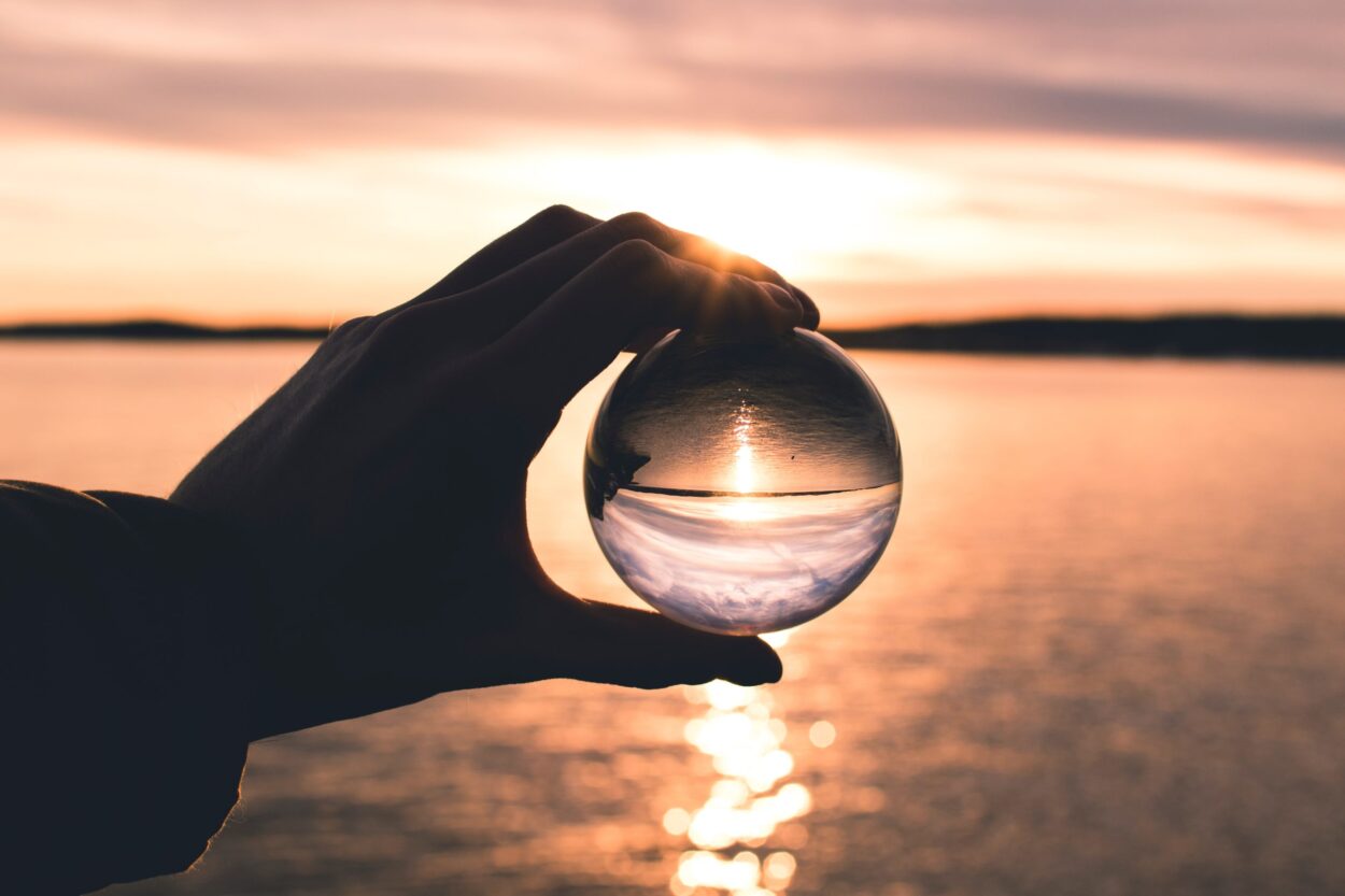 hand holding glass orb that is reflecting a sun rise over the ocean