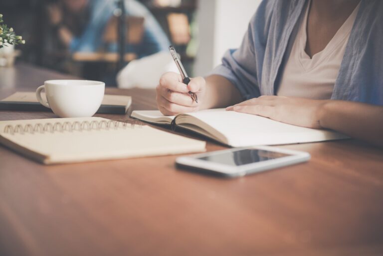 Individual sitting at desk surrounded by books, writing