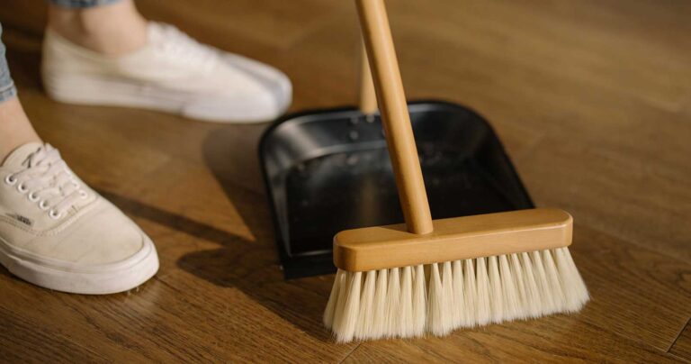pair of feet standing on a wood floor, next to a broom and dust collector