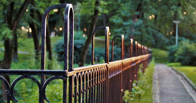 Strong black metal fence along a groomed pathway, with a park in the background.