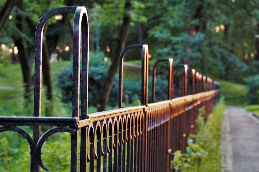 Strong black metal fence along a groomed pathway, with a park in the background.