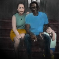 A tinted, old-style photograph of a seated couple with a toddler, smiling, by the man's feet.