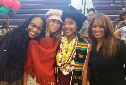Four women of varying ages pose for a photo, all trying to get close to a young woman with a kente cloth stole who has just graduated from college.