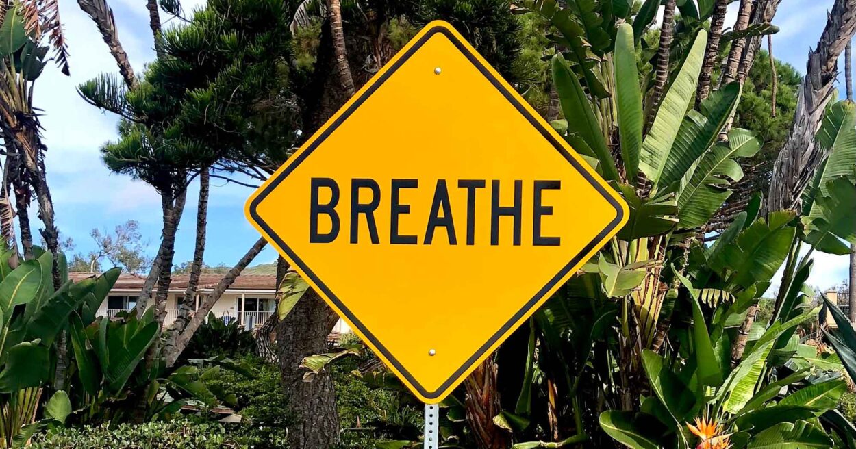 a yellow street sign that says "BREATHE"