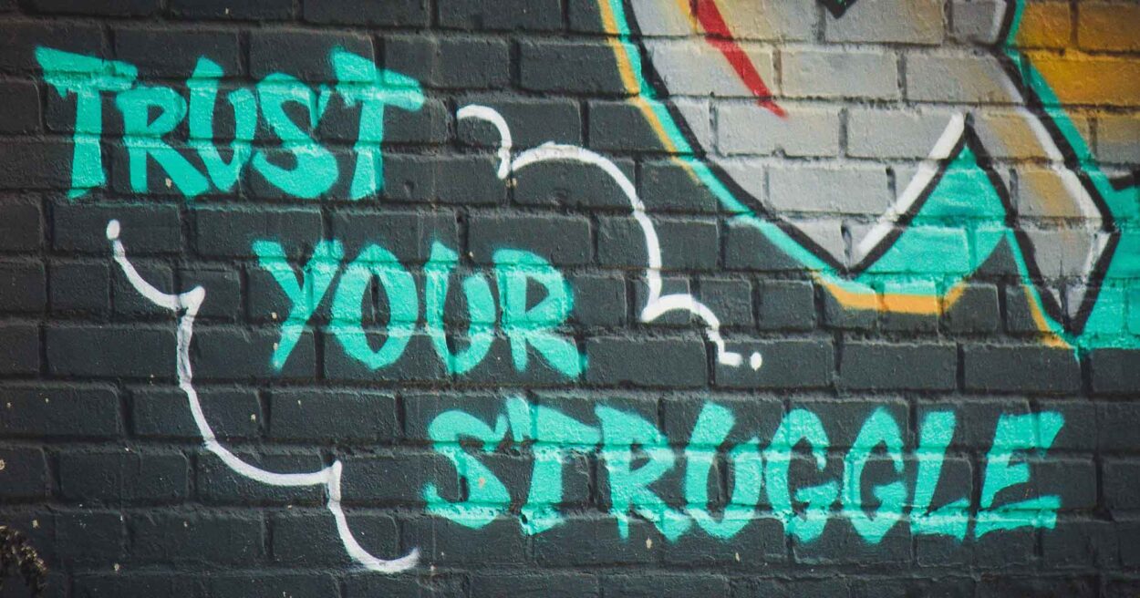 bright graffiti on a dark blue brick building that reads "Trust your struggle"