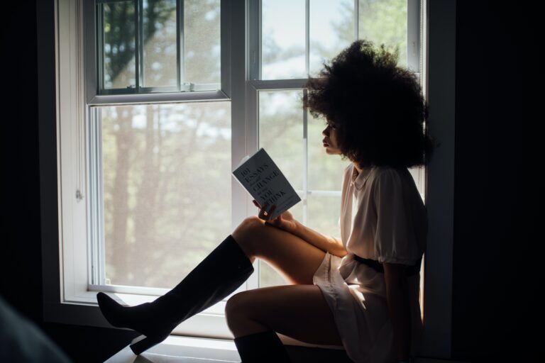woman sitting on window sill reading about about changing her thinking through literature and creative writing