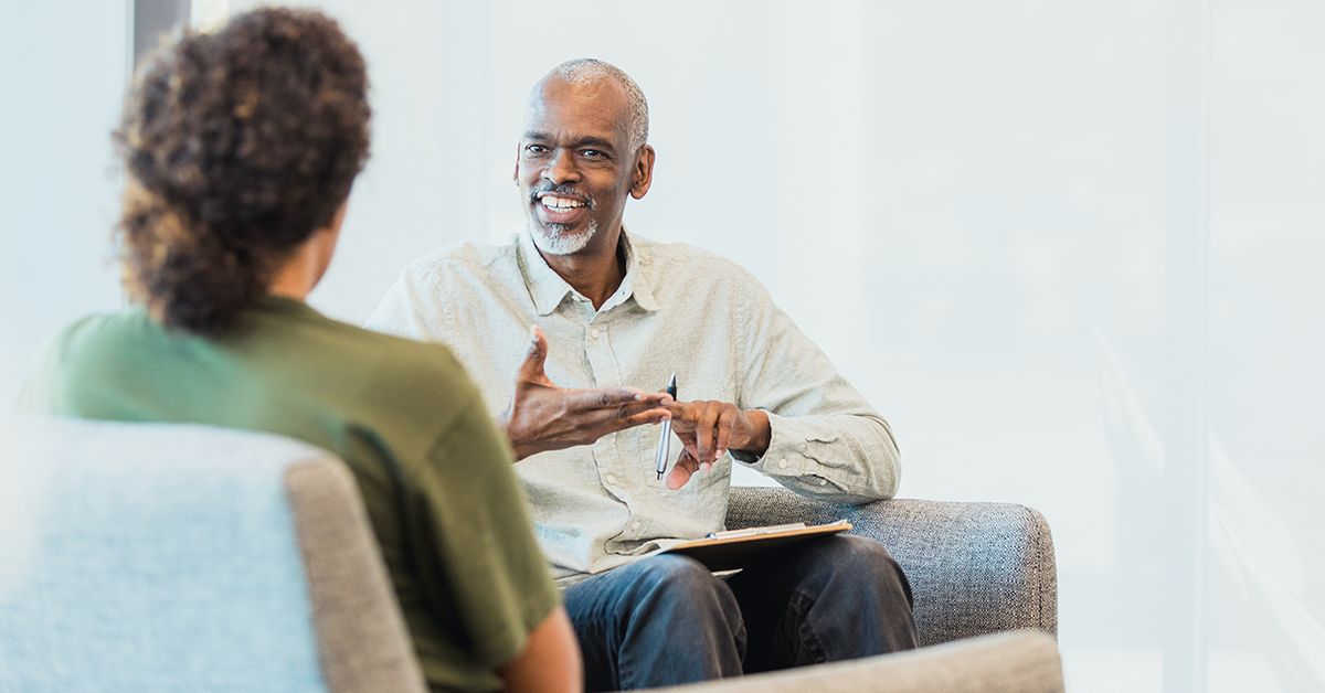 An image of a man speaking with another person, both sitting on couches, during a therapy session.