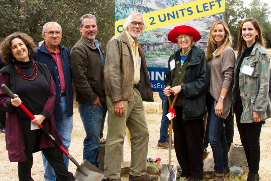 seven people standing together around a sign reporting new housing units, all smiling, some holding shovels