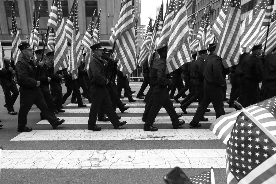 A black-and-white photograph of veterans carrying American flags in a parade.