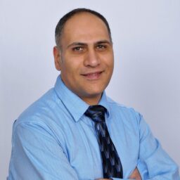 Mo Raei wearing a blue shirt and tie with arms crossed