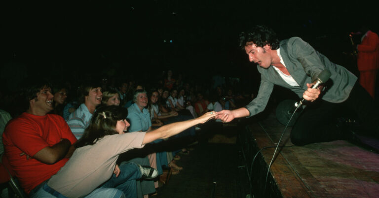 Bruce Springsteen on stage holding hands with a woman in the crowd.