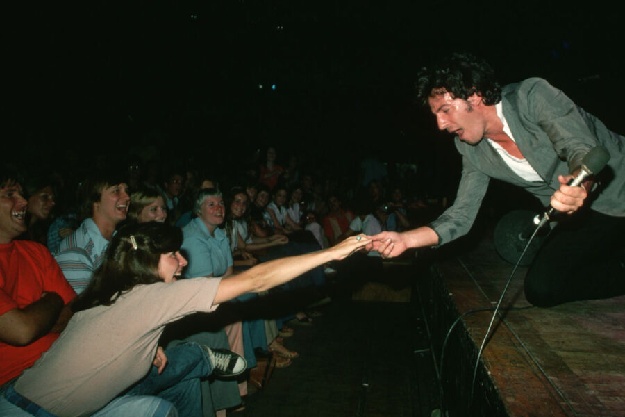 Bruce Springsteen on stage holding hands with a woman in the crowd.
