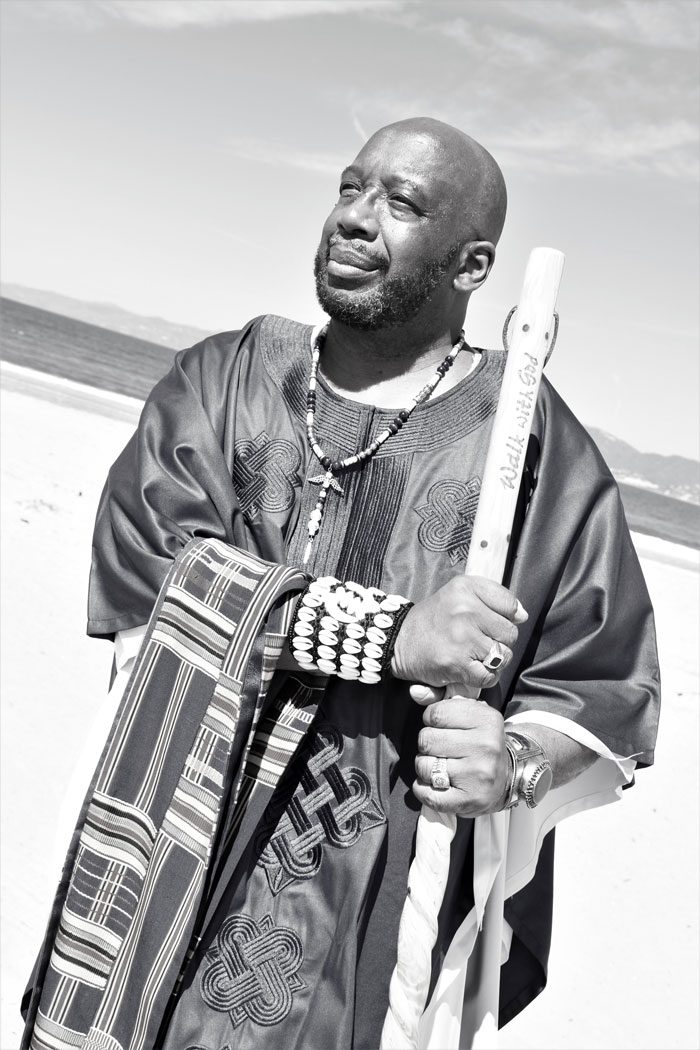 Russel Thornhill standing in traditional African garb holding a staff and looking out confidently.