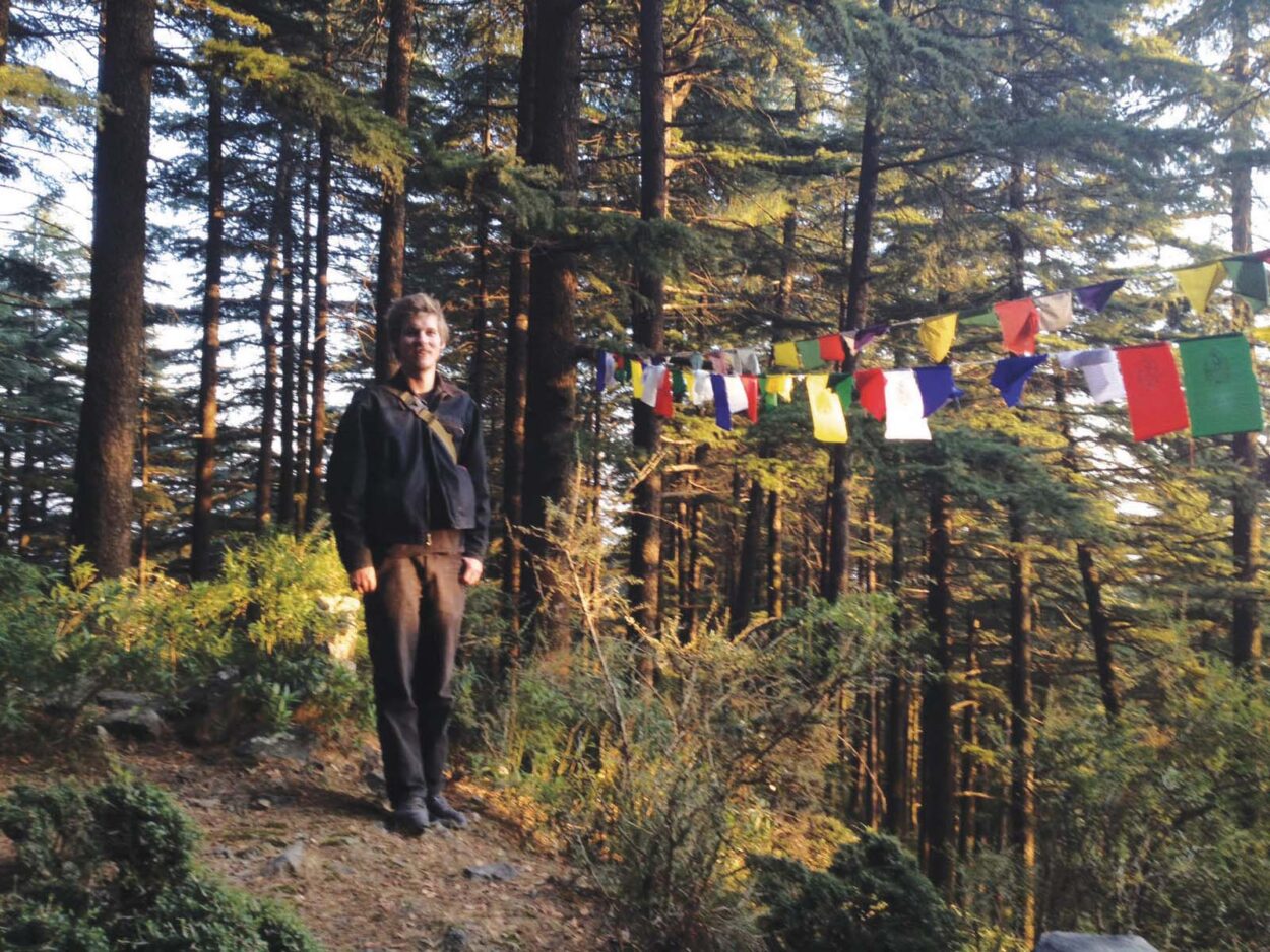 A photograph of Jasper Nighthawk in India next to prayer flags