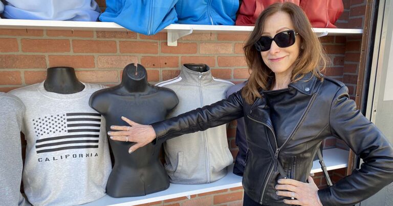 A photo of Leslie Lehr, in a leather jacket, covering up the breasts of a mannequin.