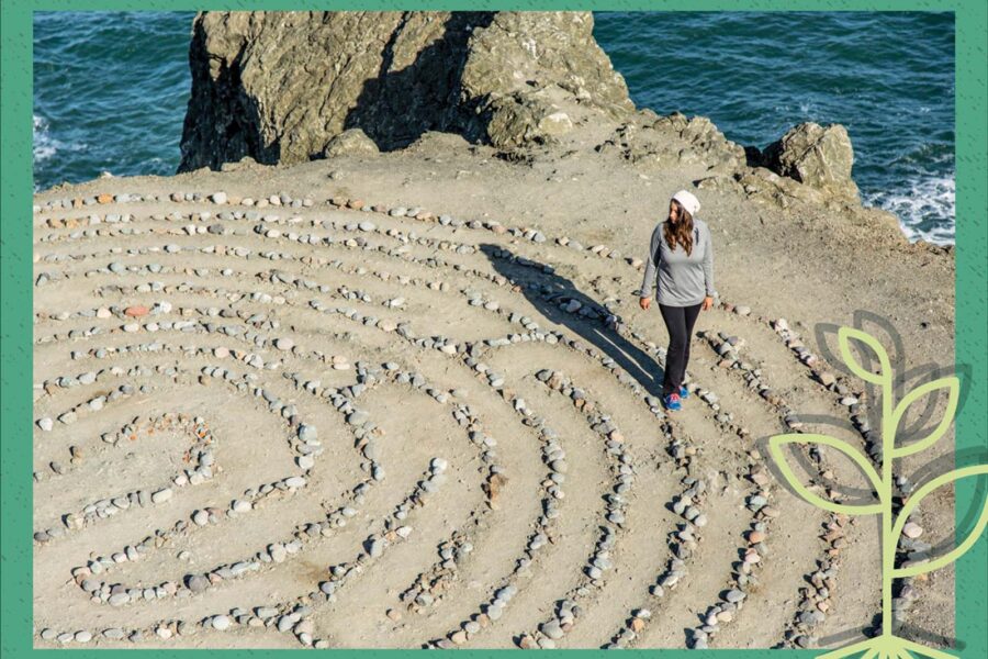 Woman walking in sand with a spiral pattern of rocks.