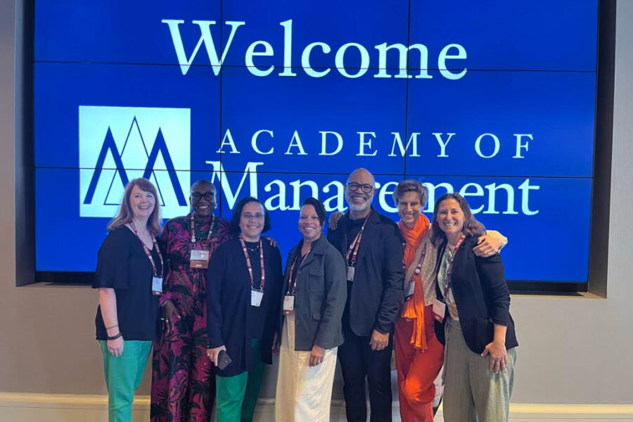 A diverse group of individuals standing in front of a large screen displaying the words "Academy of Management."