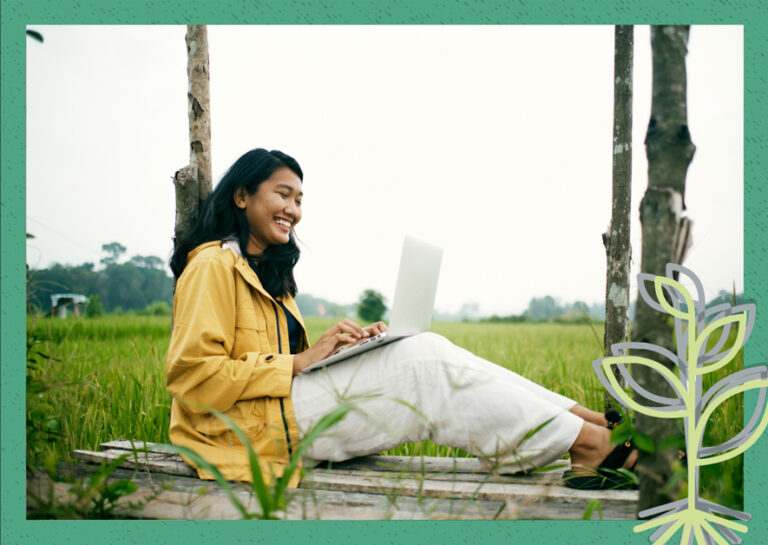 A woman sitting in a field with a laptop, enjoying the serene surroundings while working.