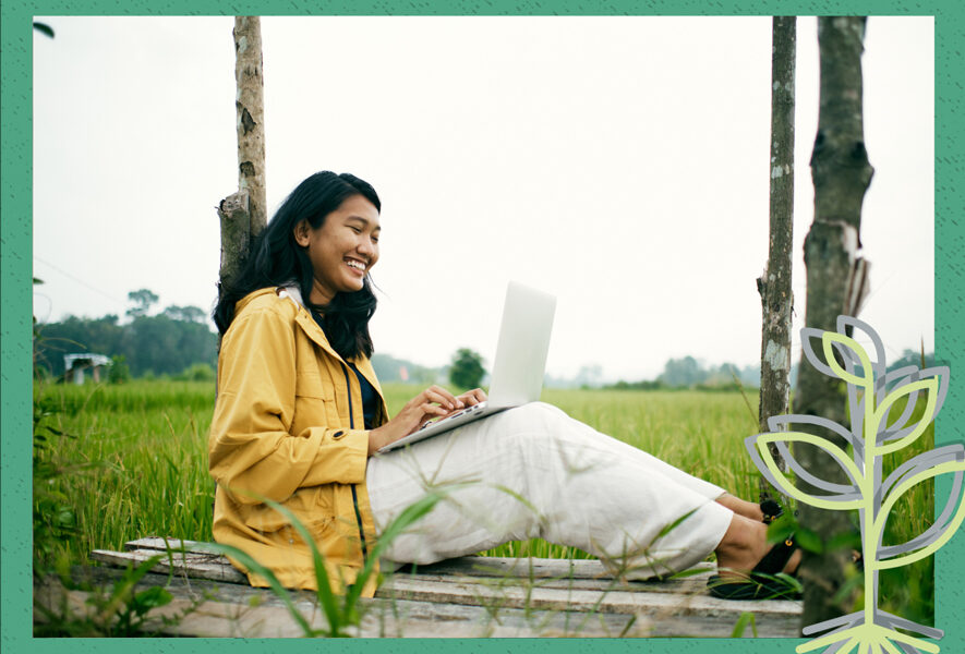 A woman sitting in a field with a laptop, enjoying the serene surroundings while working.