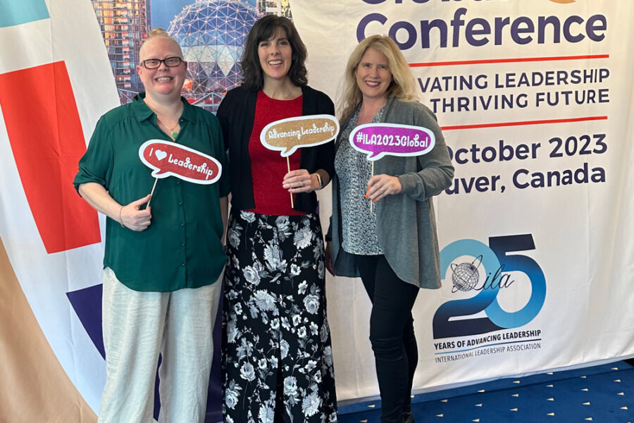 Three women holding signs in front of a banner that says global conference.