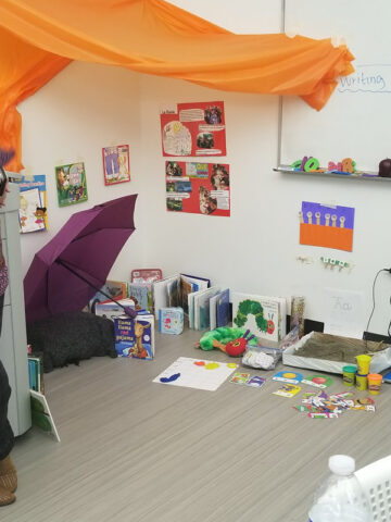Floor display of classroom items including books like The Hungry Caterpillar, a stuffed hungry caterpillar, playdoh and an umbrella.