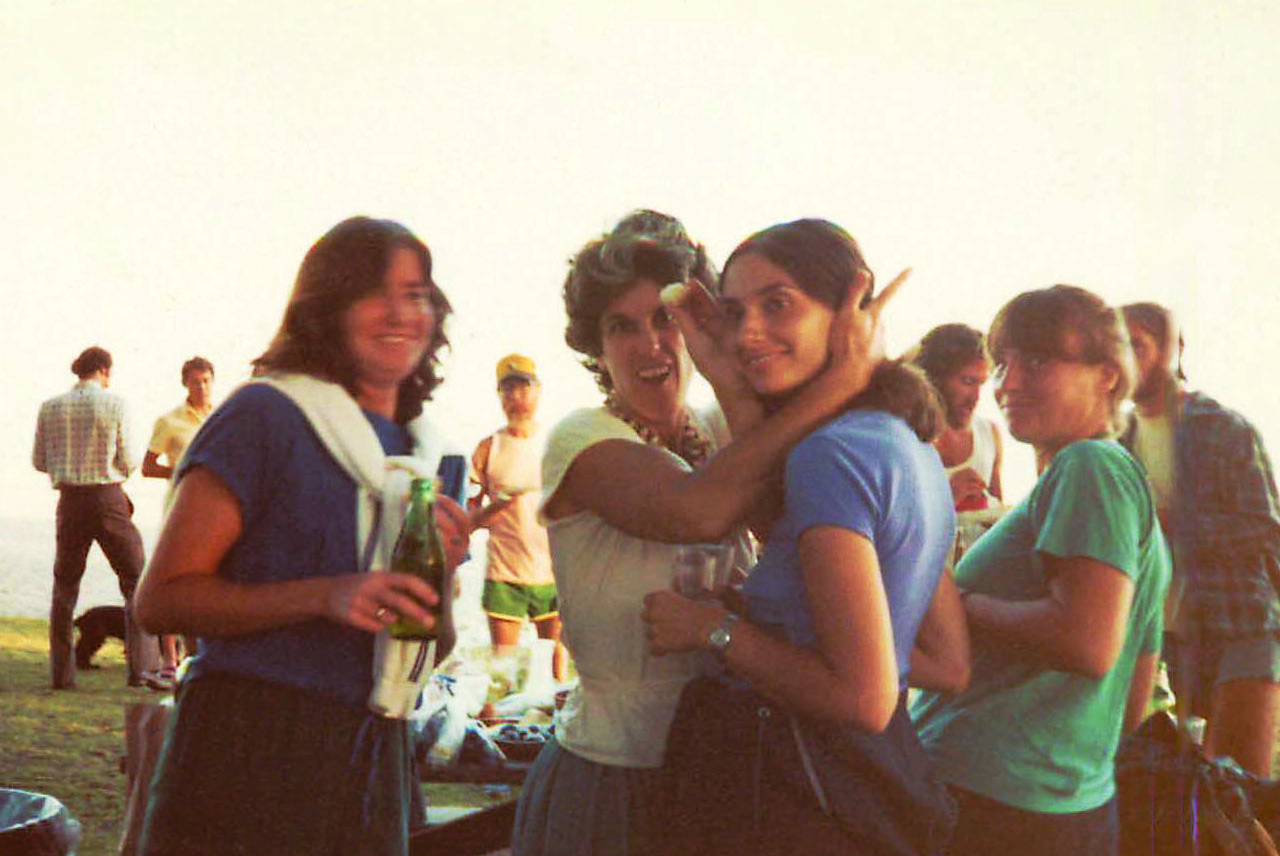 An archival photograph of people having a party at the beach, with four women posing in the foreground.