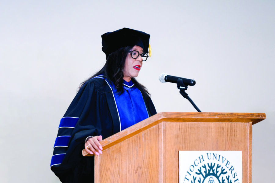 A photograph of Carol Isom-Barnes standing in full regalia at a lectern, giving a graduation speech.
