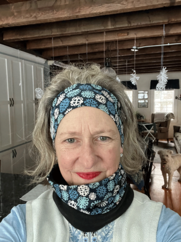 Maura Hart, A woman with a blue and white scarf wrapped around her neck, looking elegant and stylish.