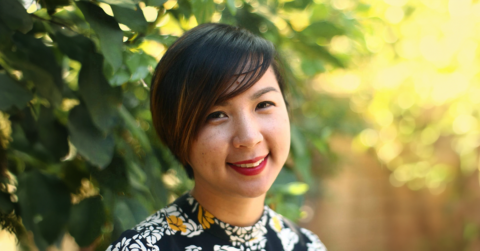 A photo of Cathy Linh Che standing outside in front of some plants.