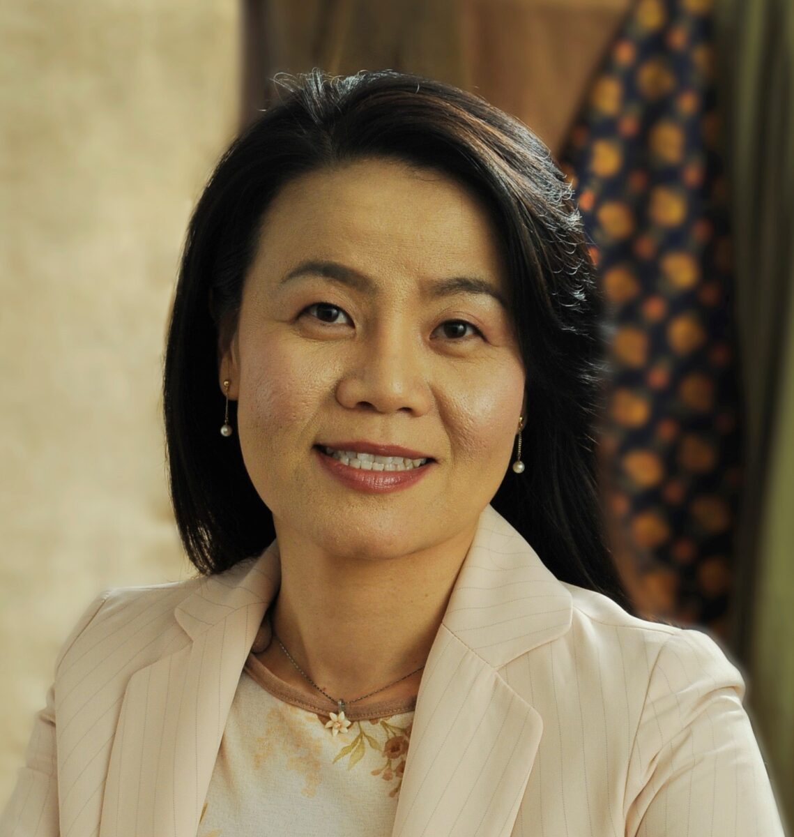 A photo fo MAria Kim, smiling and wearing dangling earrings and a white blazer.
