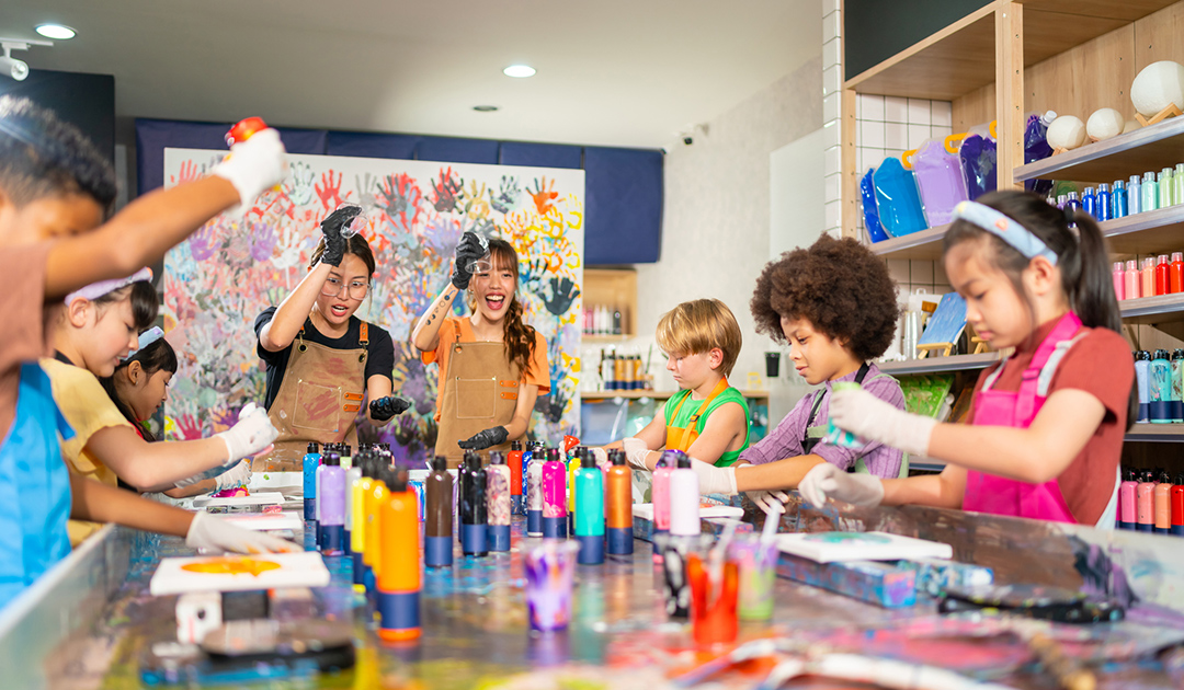 Children engaged in painting activities at a table in a vibrant classroom setting.