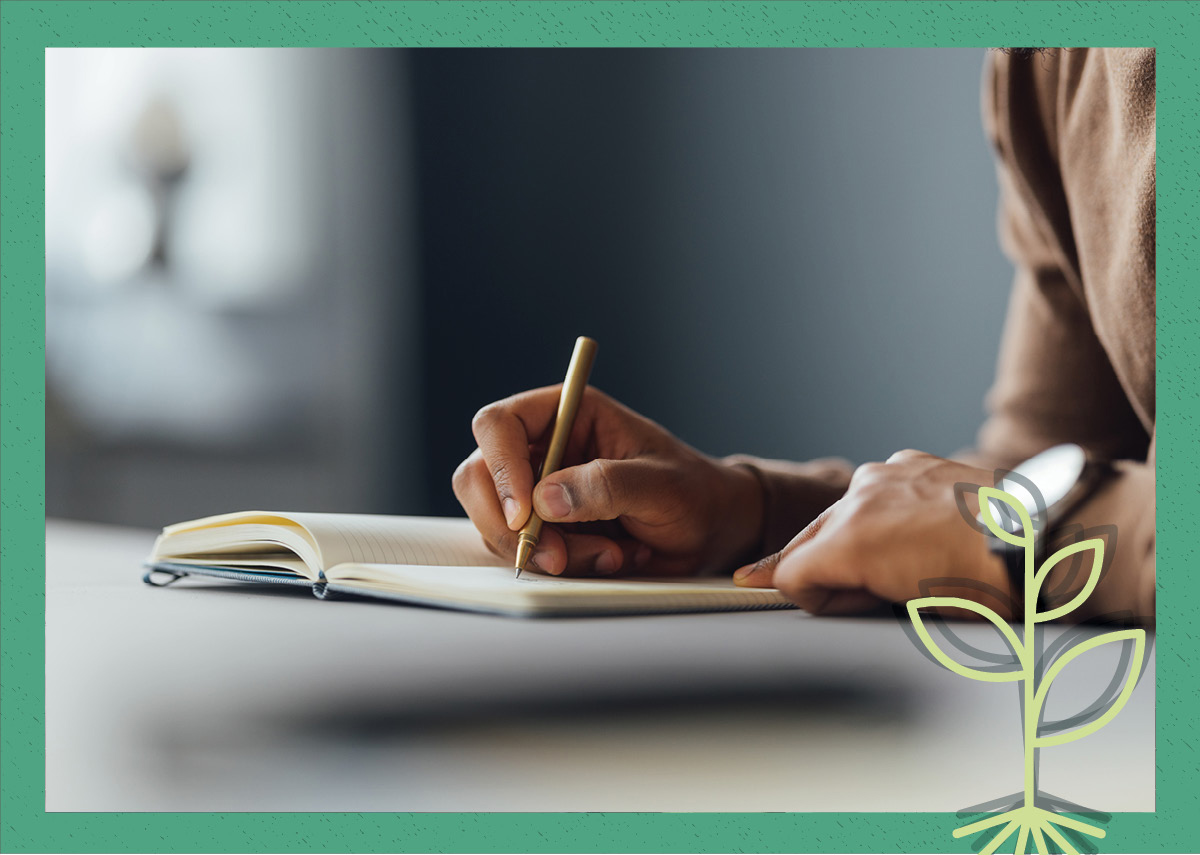 A person writing on a desk in a journal.