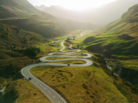 A curvy road through the mountains with cars on the road.