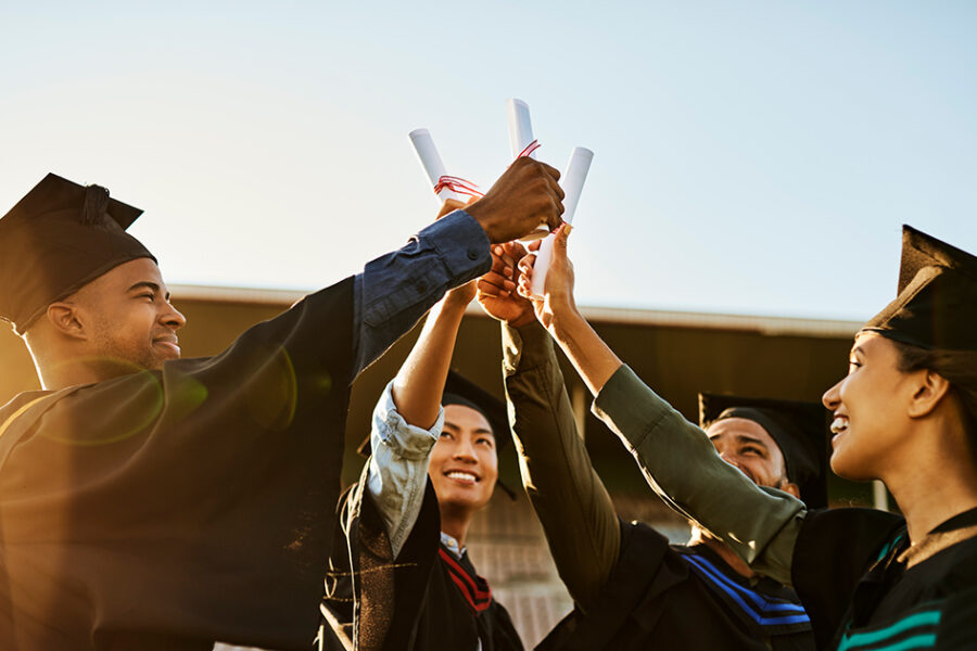 A group of 4 graduates with their hands and diplomas up and meeting in the middle of the circle.