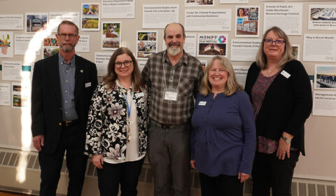 A group of people stands together in front of a wall displaying various pictures.