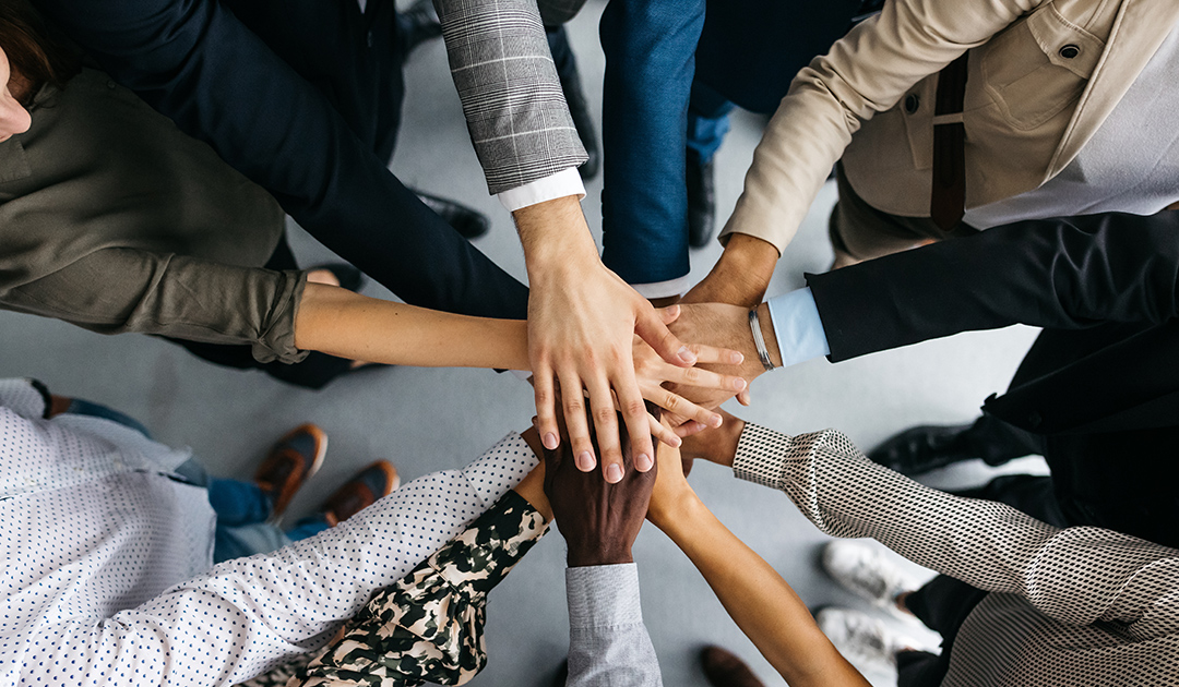 A diverse group of business people standing in a circle, joining hands in a show of unity and collaboration.