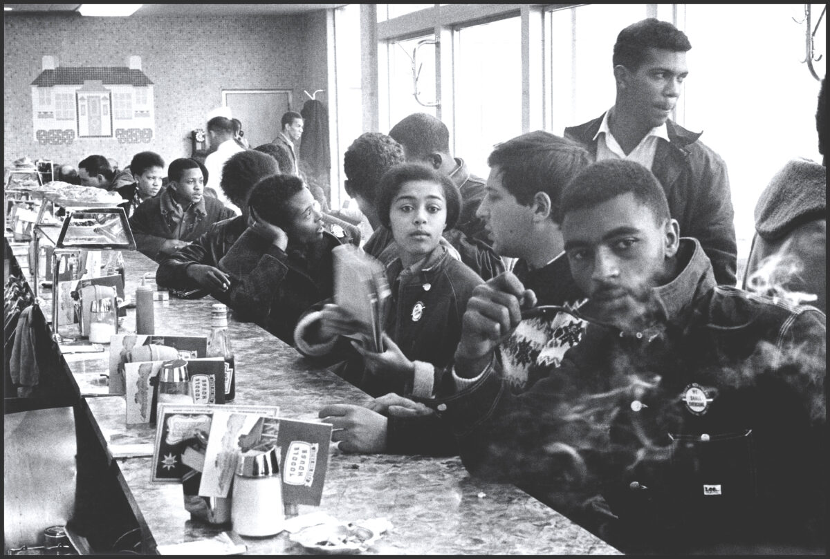 An archival photograph of Judy Richardson as a young woman, sitting at a lunch counter along with many fellow protesters as part of a sit-in.