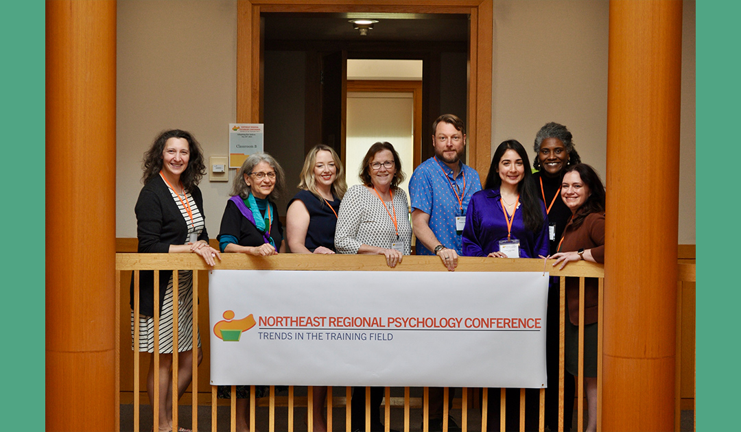 A diverse group of people stands in front of a banner reading Northeast Regional Psychology Conference.