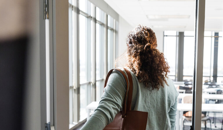 A rear view of a female student holding the door as she enters an empty classroom before her class starts.