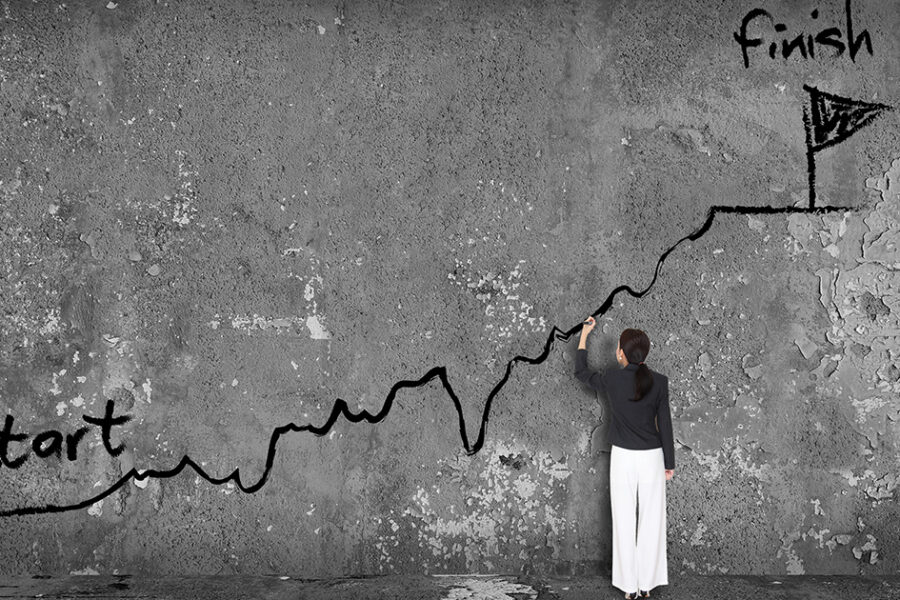 A woman standing in front of a concrete wall drawing a line with start at one end and finish at the other.