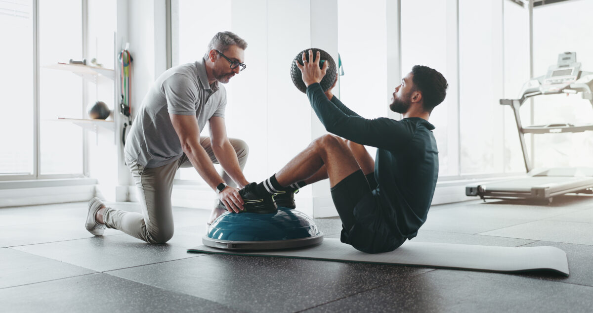 Two people are exercising together on a gym floor, demonstrating various fitness routines.
