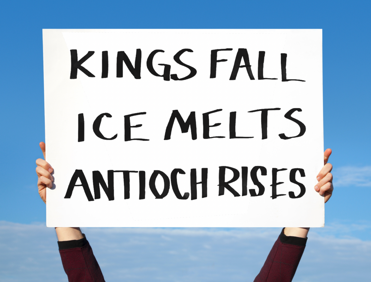Hands hold up a large white protest sign against a blue sky reading, “KINGS FALL / ICE MELTS / ANTIOCH RISES.