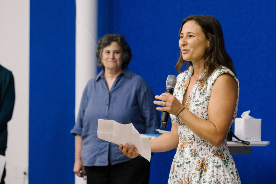 An image of Ileya Grosman standing on stage holding a microphone and speaking during a GSLC commencement