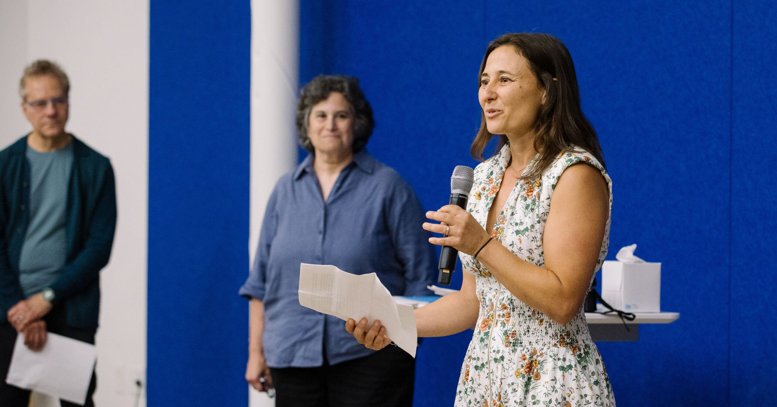 An image of Ileya Grosman standing on stage holding a microphone and speaking during a GSLC commencement