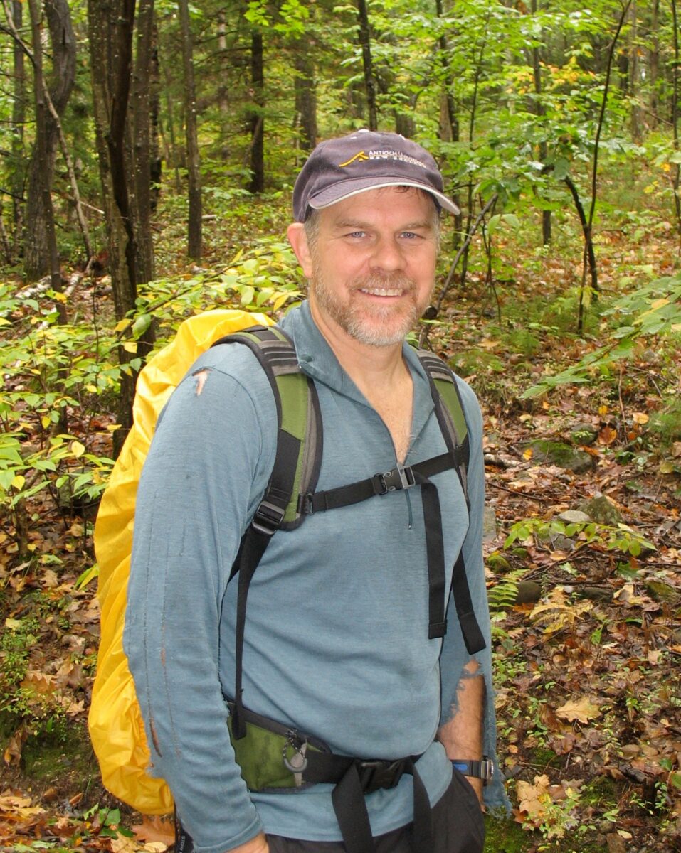 Peter Palmiotto outdoors in a forest setting, carrying a backpack during a field hike.