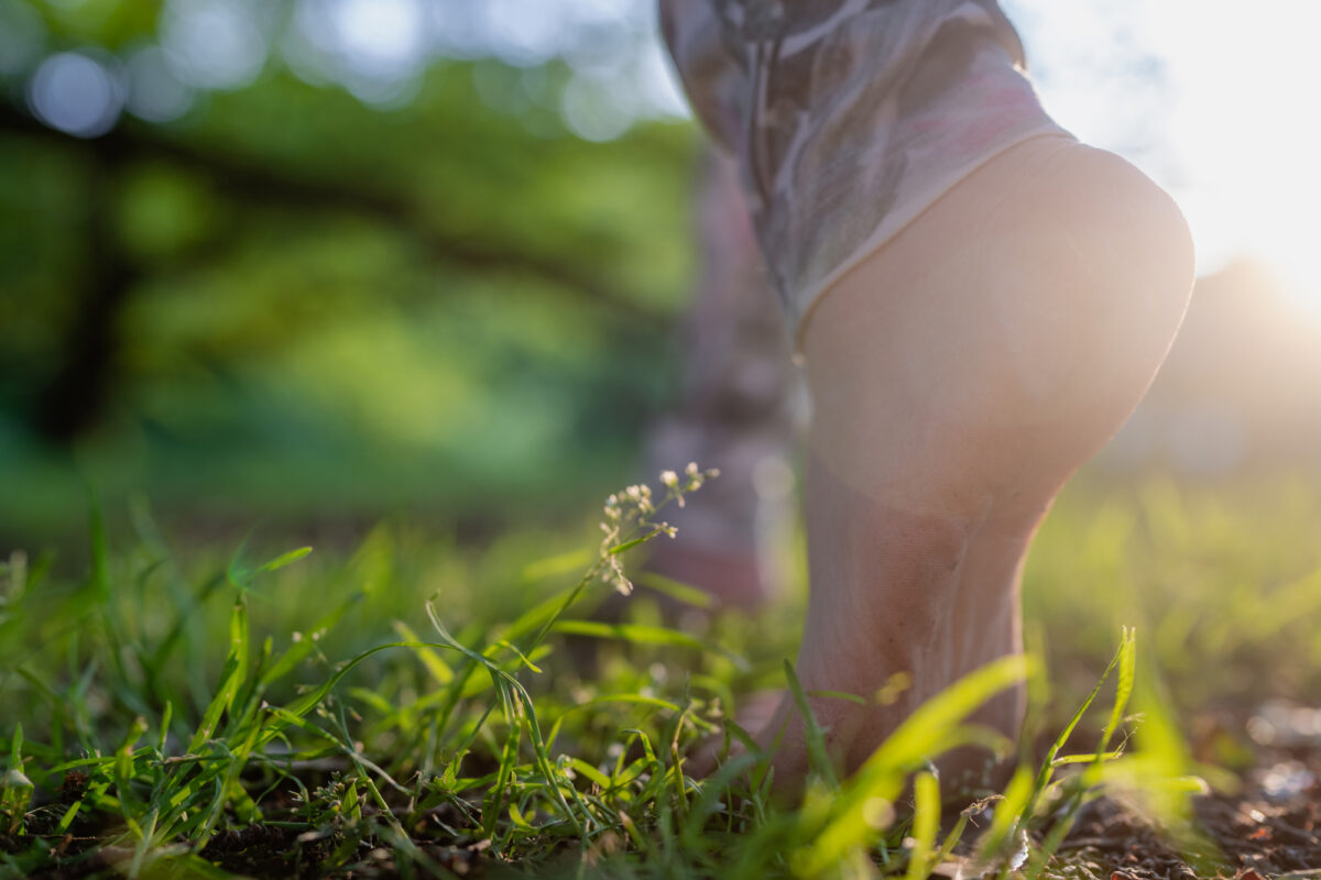 Bare feet walking in green grass with sunlight filtering through