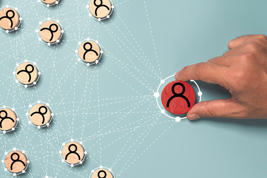 A hand selecting a highlighted red person icon within a connected network of smaller user icons, representing leadership or influence.