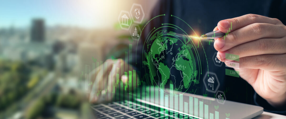 Person using a digital interface with global sustainability graphics, financial growth charts, and environmental icons over a laptop screen.