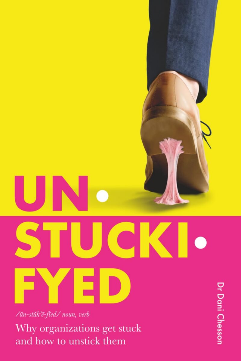 Book cover for Unstuckifyed by Dr. Dani Chesson. A brown dress shoe steps forward with pink chewing gum stuck to its sole against a bright yellow background. The lower half is hot pink with large yellow title text and the subtitle, “Why organizations get stuck and how to unstick them.”