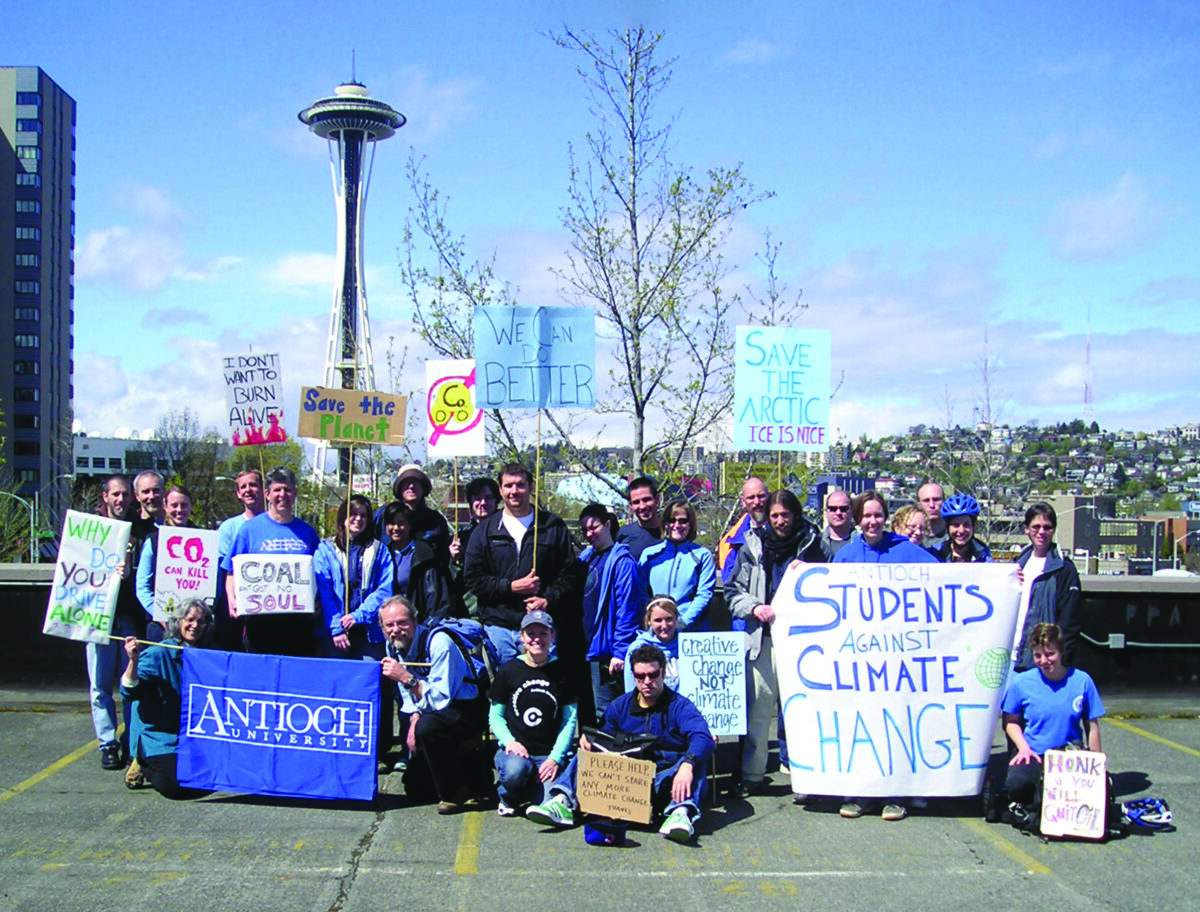 Group of students and activists at a climate-change rally holding handwritten signs; Space Needle visible in Seattle skyline behind them.